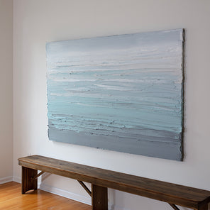 An abstract painting with turquoise impasto brushstrokes in a color gradient is seen at an angle in the artists studio.