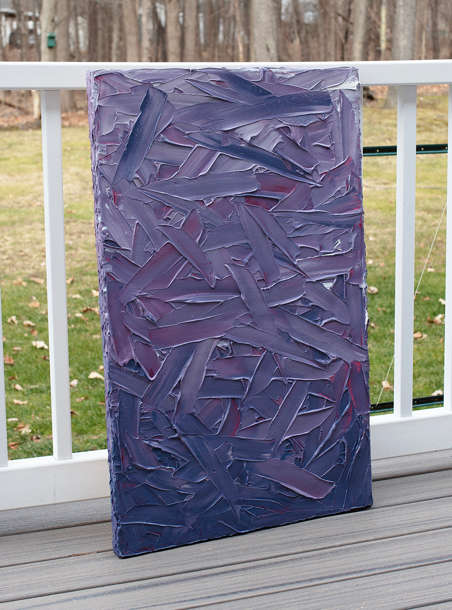 A tonal purple and pink thickly textured abstract painting by Teodora Guererra leans on a deck outside in the natural light.