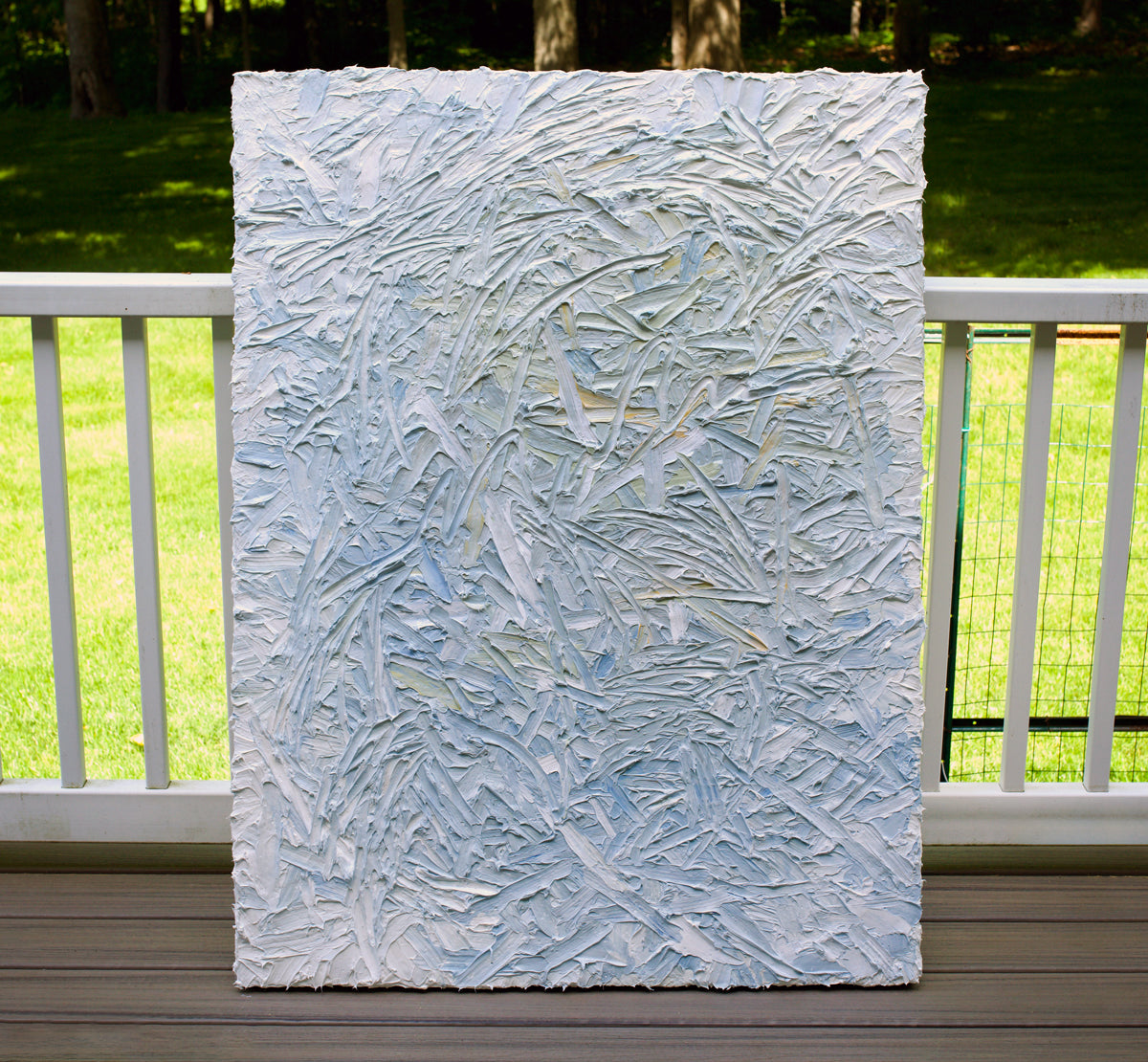 Textured abstract painting on a wooden deck with grass and trees in the background