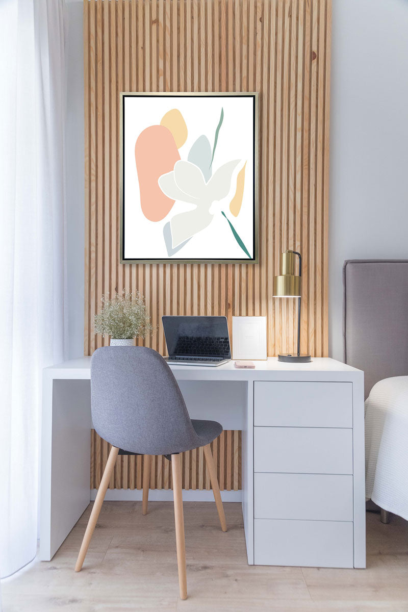 A light abstract botanical art print framed in a white frame hangs on a wood paneled wall above a desk and bed. 