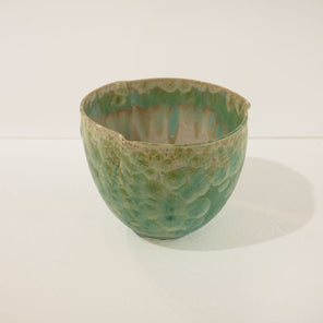 A green ceramic bowl rests on a white surface in front of a white wall. 
