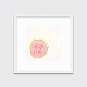 An abstract art print of a fruit framed in a white frame hangs on a light wall. 