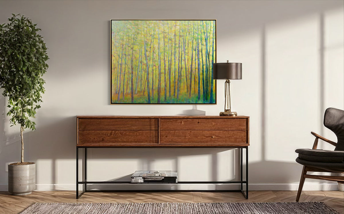 An abstracted yellow painting of forest trees hangs on a beige wall above a dark wood modern credenza with a chair on one side and a potted plant on the other. 