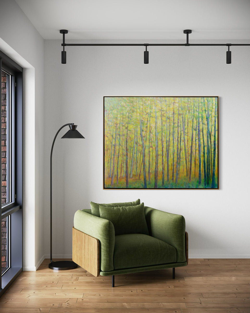 An abstracted yellow painting of forest trees hangs on a white wall above a green chair.