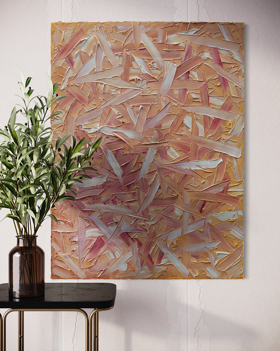 A orange, pink, coral and white thickly textured abstract painting hangs on a white wall.  Sitting in front is a black marble table with brass legs.  On the table sits an amber glass vase with eucalyptus branches.