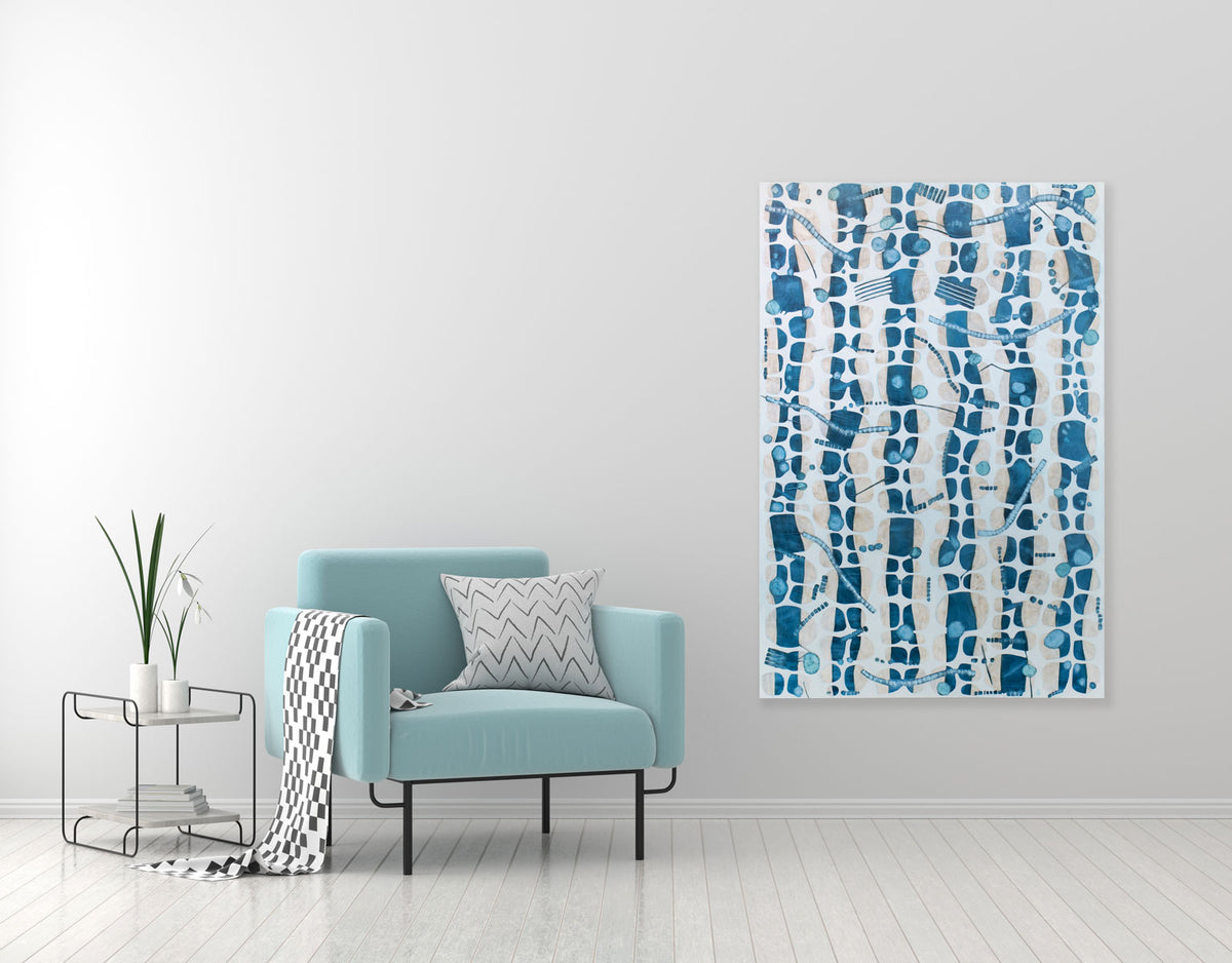 An abstract blue and white painting hangs on a light wall next to a modern turquoise armchair with black and white throw pillow and blanket, and side table. 