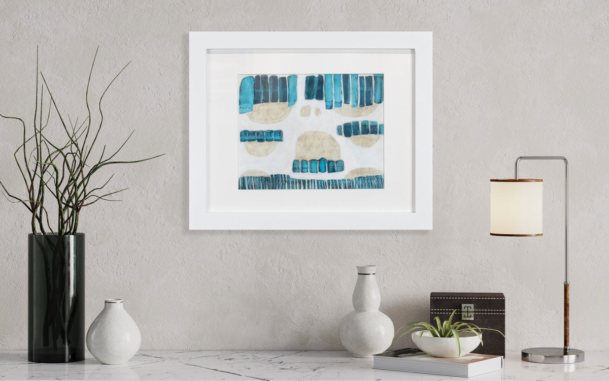 A blue, beige, and white abstract painting framed in a white frame hangs on a textured wall above a marble console table with modern decor on the surface, including a succulent plant, a book, and table lamp. 