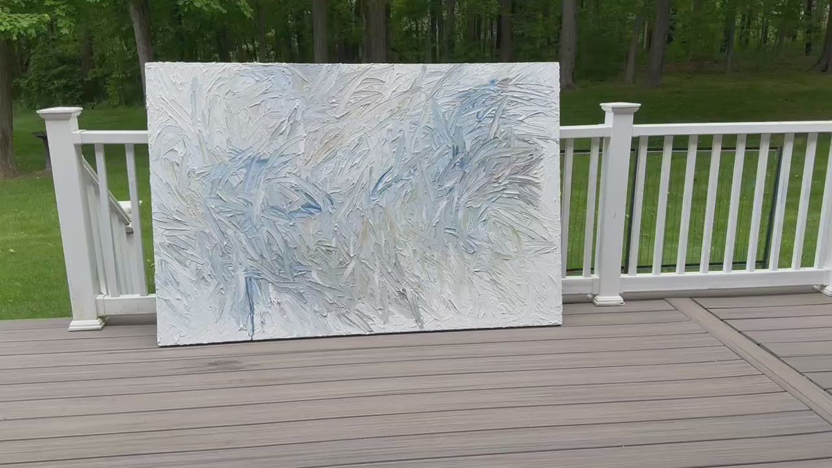 A video of an original abstract painting by Teo Guererra with blue and gray tones on a wooden deck at her studio.
