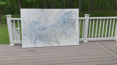 A video of an original abstract painting by Teo Guererra with blue and gray tones on a wooden deck at her studio.
