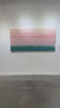 A video of a peach, orange, coral, pale pink and teal thickly textured abstract painting hangs on a white wall.