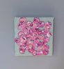 A video of a very textured abstract painting with celadon background and circle type abstract flowers in pink, peach, plum and white hangs on a white wall.