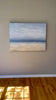 A video of a very textured coastal painting with a lone sailboat hangs on a wall.