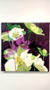 A Video of a Floral painting with white, green, and purple flowers on a dark background hanging on a wall.