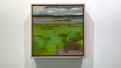 A blue and green framed textured abstracted landscape painting hangs on a white wall.