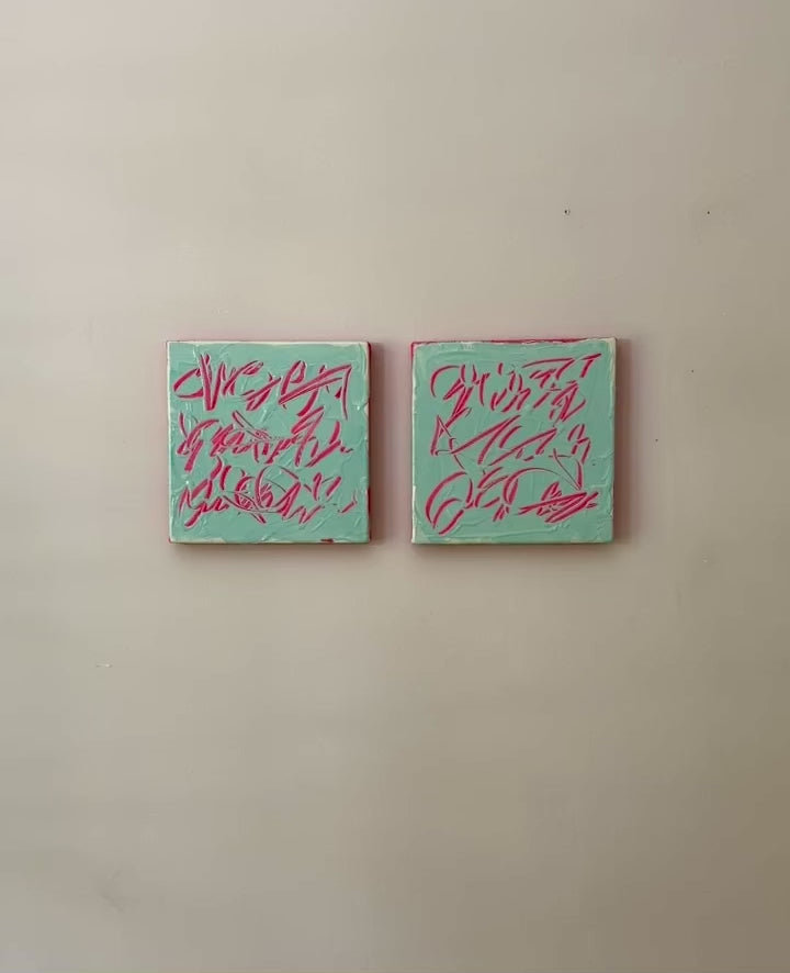 A video of two square abstract text based paintings hanging side by side on a textured off-white wall. 