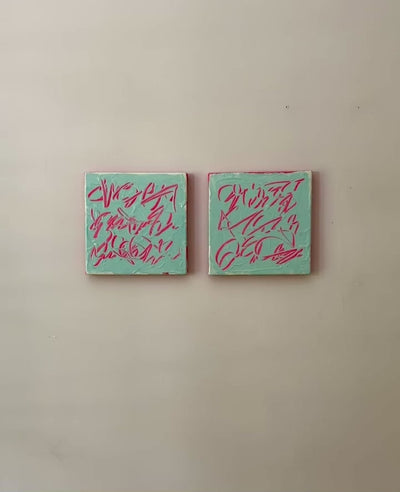 A video of two square abstract text based paintings hanging side by side on a textured off-white wall. 