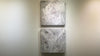 A video of a pair of thickly textured paintings in grey, white, blue grey and plum grey by Teodora Guererra hanging on a white wall.