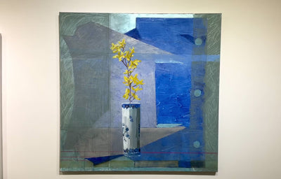 An abstracted blue painting with a vase with yellow flowers in the foreground hangs on a white wall.