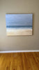 A video of an abstracted coastal seascape painting hangs on a grey wall.  Edit alt text