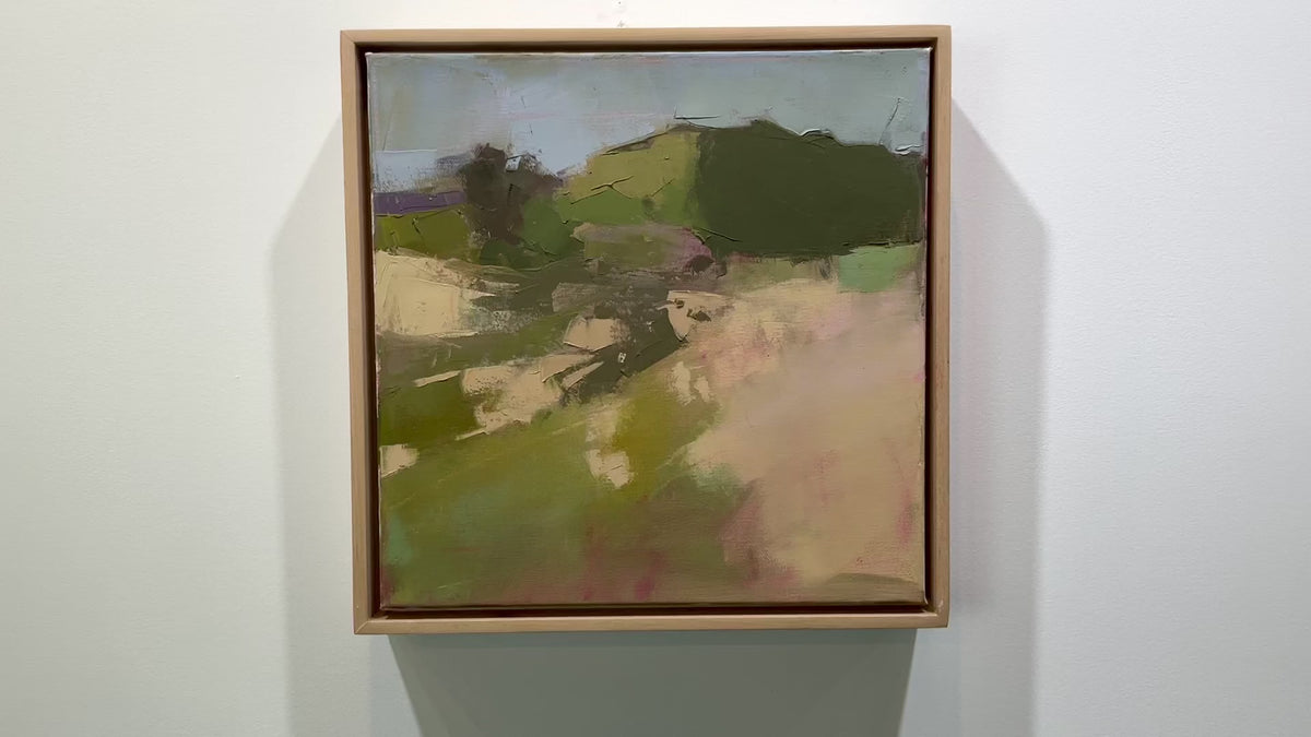 A framed green and warm beige abstracted landscape painting hangs on a white wall.