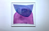 A blue and magenta minimalist abstract watercolor painting framed in a white frame hangs on a white wall.