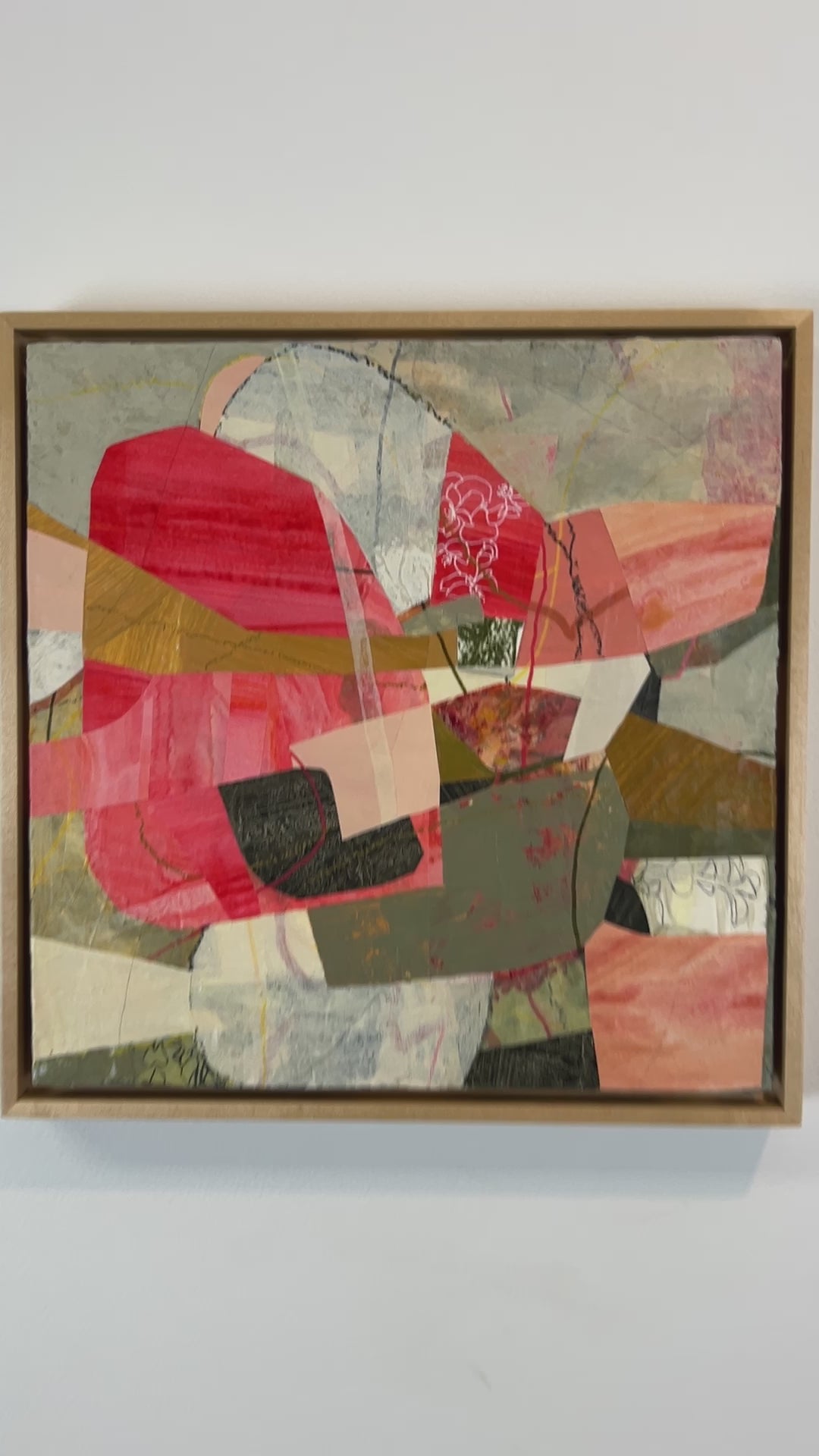 A video of a framed abstract collage artwork featuring geometric shapes in shades of red, beige, and green, with a white background hanging on a white wall.