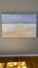 An abstracted coastal seascape painting hangs on a grey wall.
