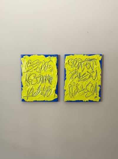 A video of two abstract text based painting featuring a thick, yellow-green impasto texture with blue abstract scribbled lines and a bright blue base hanging on a wall.