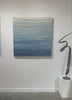 A video of a blue, beige, lavender and light yellow textured abstract painting by Teodora Guererra hangs on a white wall.