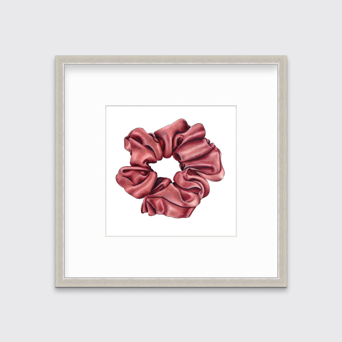 A drawing of a pink hair scrunchie framed in a silver frame hangs on a white wall. 