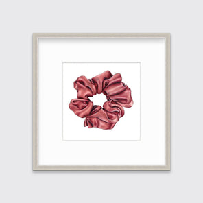 A drawing of a pink hair scrunchie framed in a silver frame hangs on a white wall. 