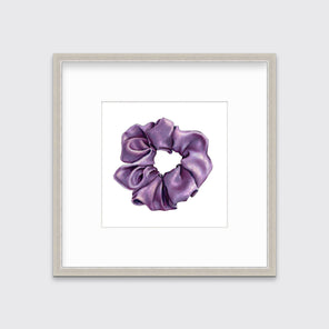 A drawing of a purple hair scrunchie, framed in a silver frame hangs on a white wall. 