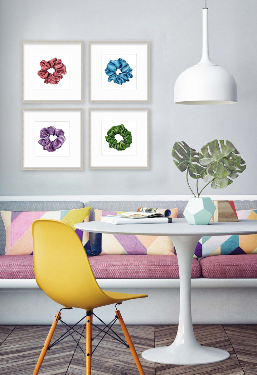Four drawings of scrunchies in different colors hangs on a light grey wall above a colorful bench sofa chair, midcentury white table and yellow seat.
