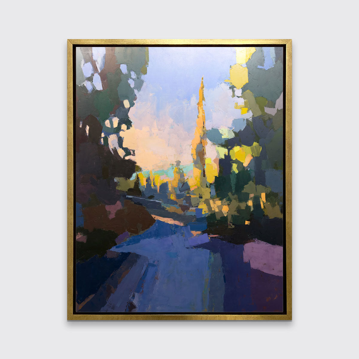 A blue abstract landscape art print framed in a gold frame hangs on a white wall.