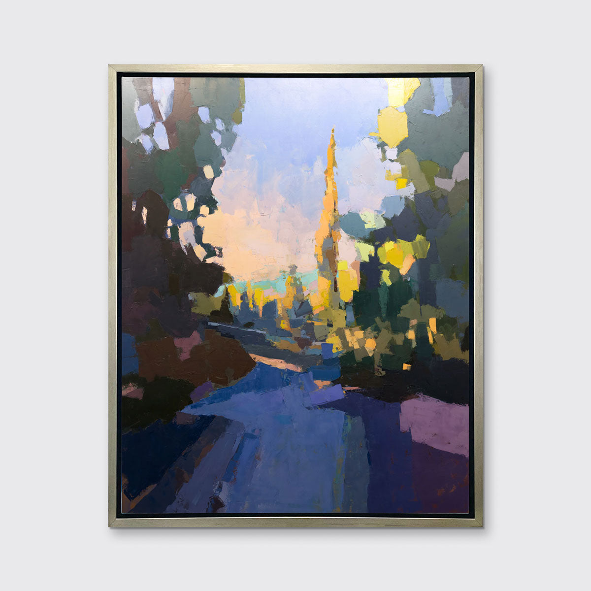 A blue abstract landscape art print framed in a silver frame hangs on a white wall. 