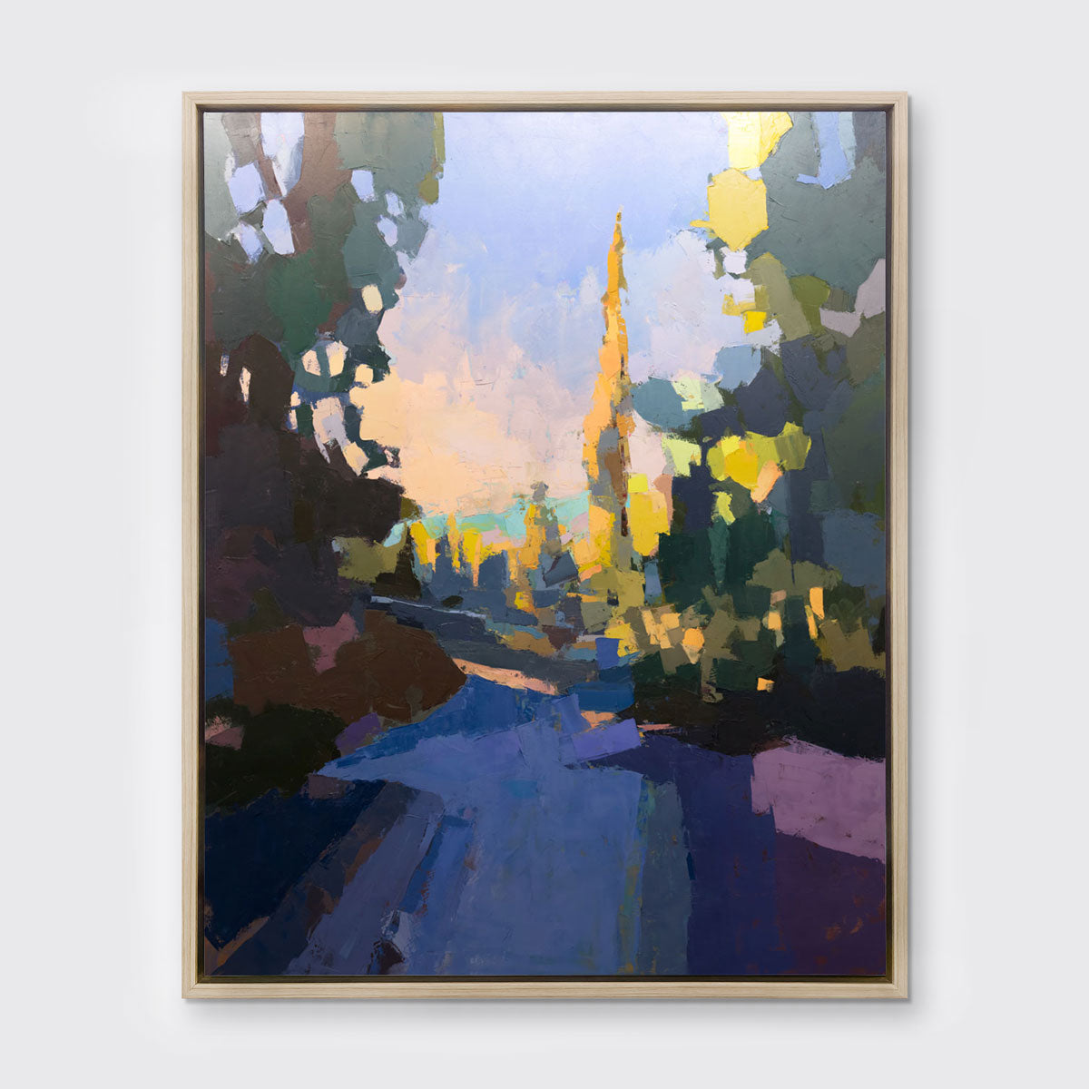 A blue abstract landscape art print framed in a white oak frame hangs on a white wall.