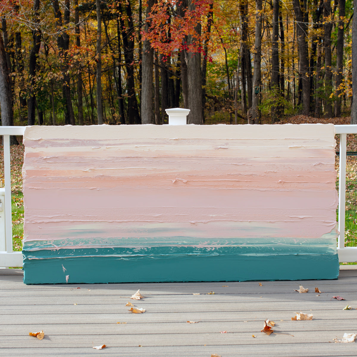 A peach, coral, pale pink and teal thick textured painting leaning outside on a deck in natural light of a painting by Teodora Guererra.