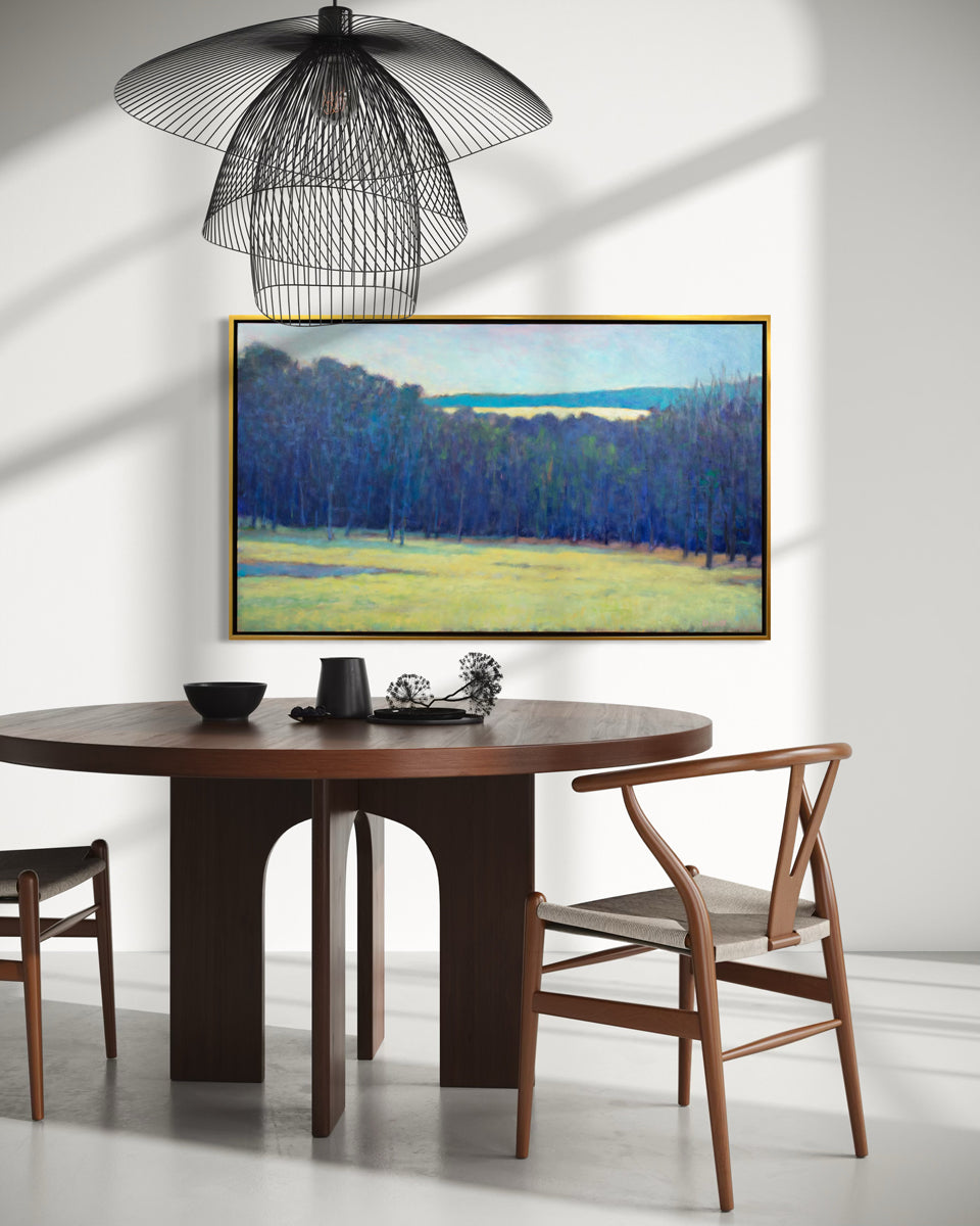 Dining room with wooden table, chairs, and a framed landscape painting on the wall.