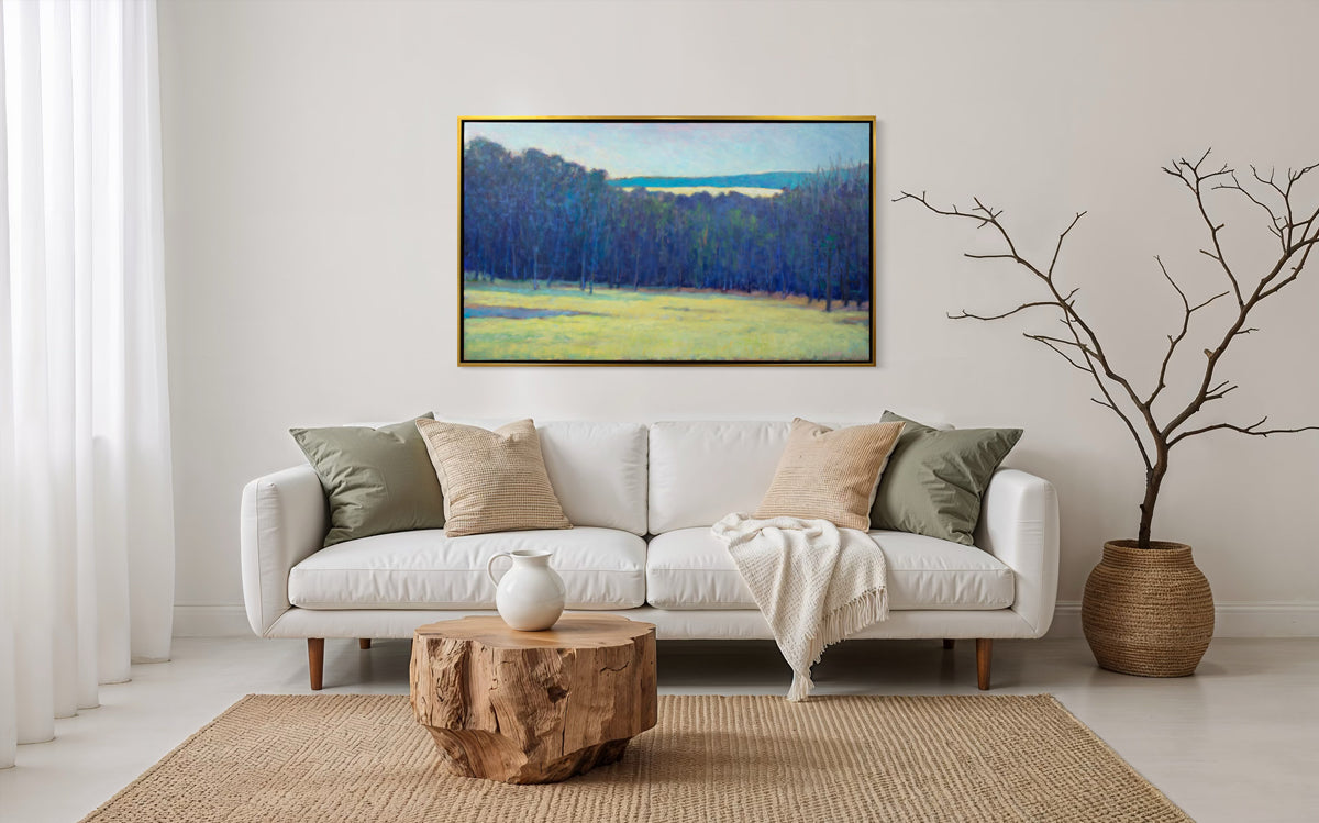 Living room with a white sofa, wooden coffee table, and framed landscape painting on the wall.