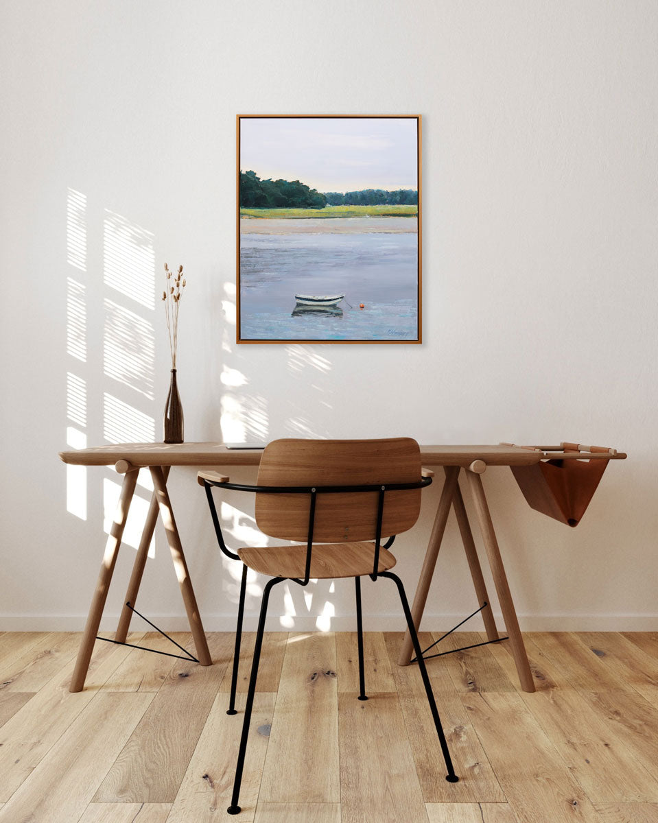 A light seascape painting hangs on a white wall above a minimalist wood desk and chair. 