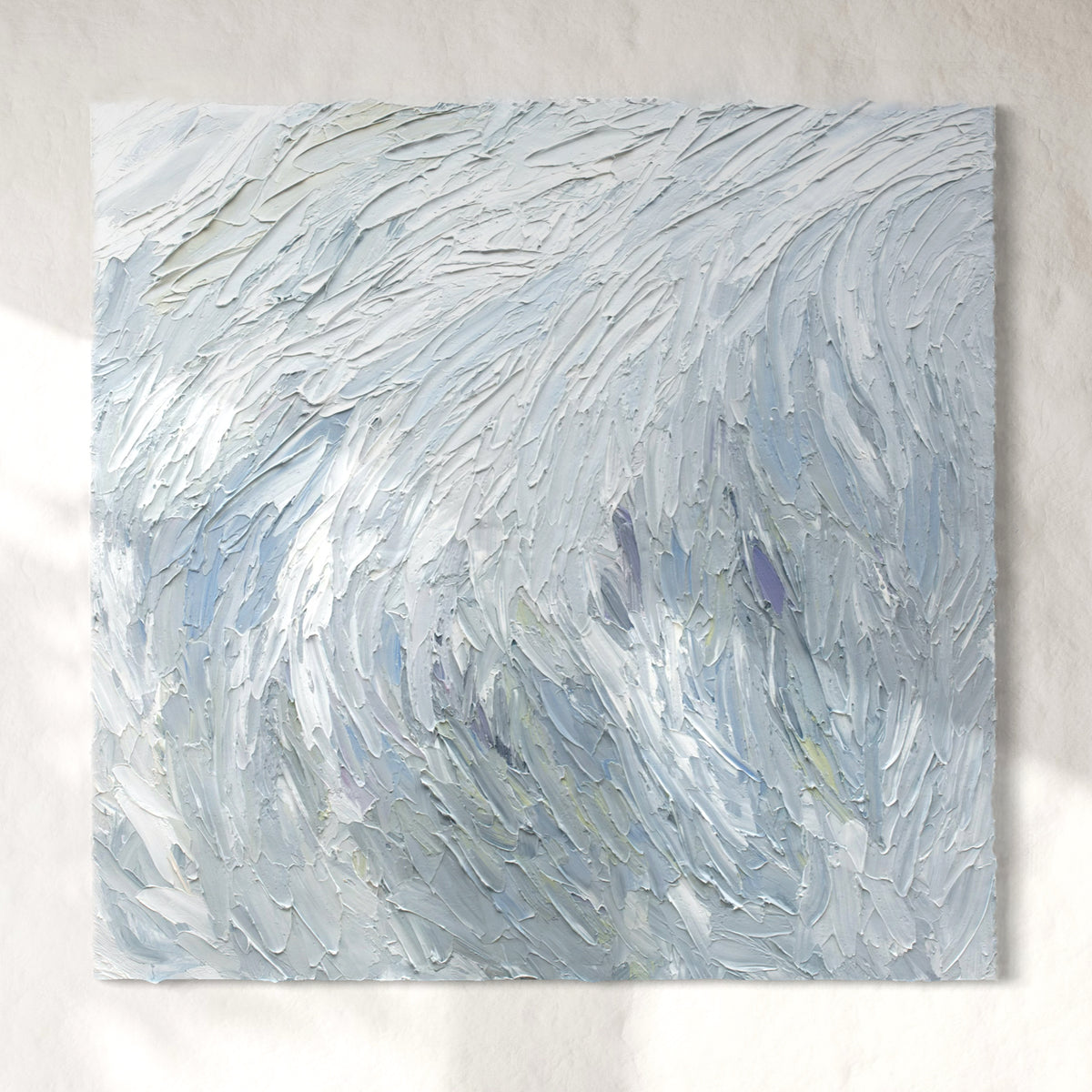 A Grey blue, light blue, lavender, celadon and white thickly textured abstract painting hanging on a white wall in natural light by Teodora Guererra.