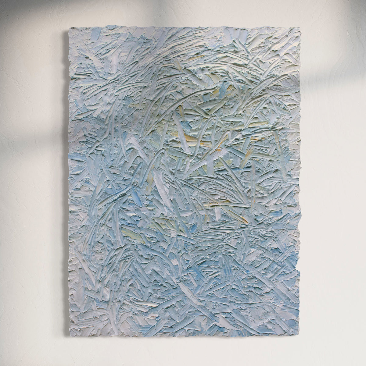 Original abstract textured painting with blue and white tones hanging on a sun light white wall.