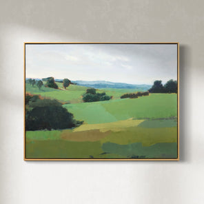 A green landscape painting framed in a light wood floater frame hangs on a white wall. 