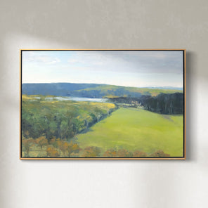 A yellow-green landscape painting in a light wood frame hangs on a light wall.