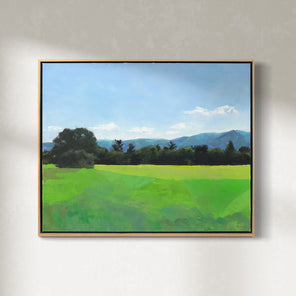 A blue and green landscape painting in a wood frame hangs on a white wall. 