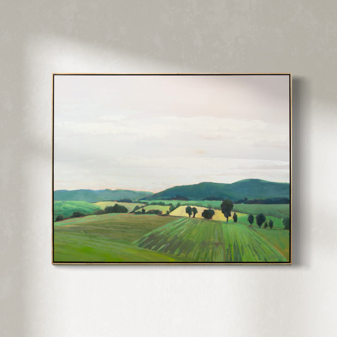 A taupe, yellow and green landscape painting by Molly Doe Wensberg hangs in a light wood floater frame on a white wall.
