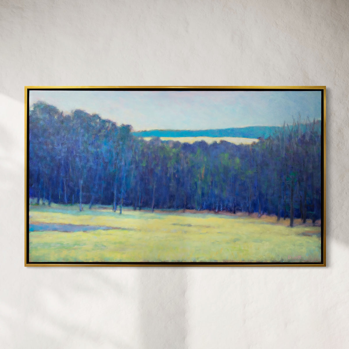 Framed painting of a landscape with trees and a field on a white wall.