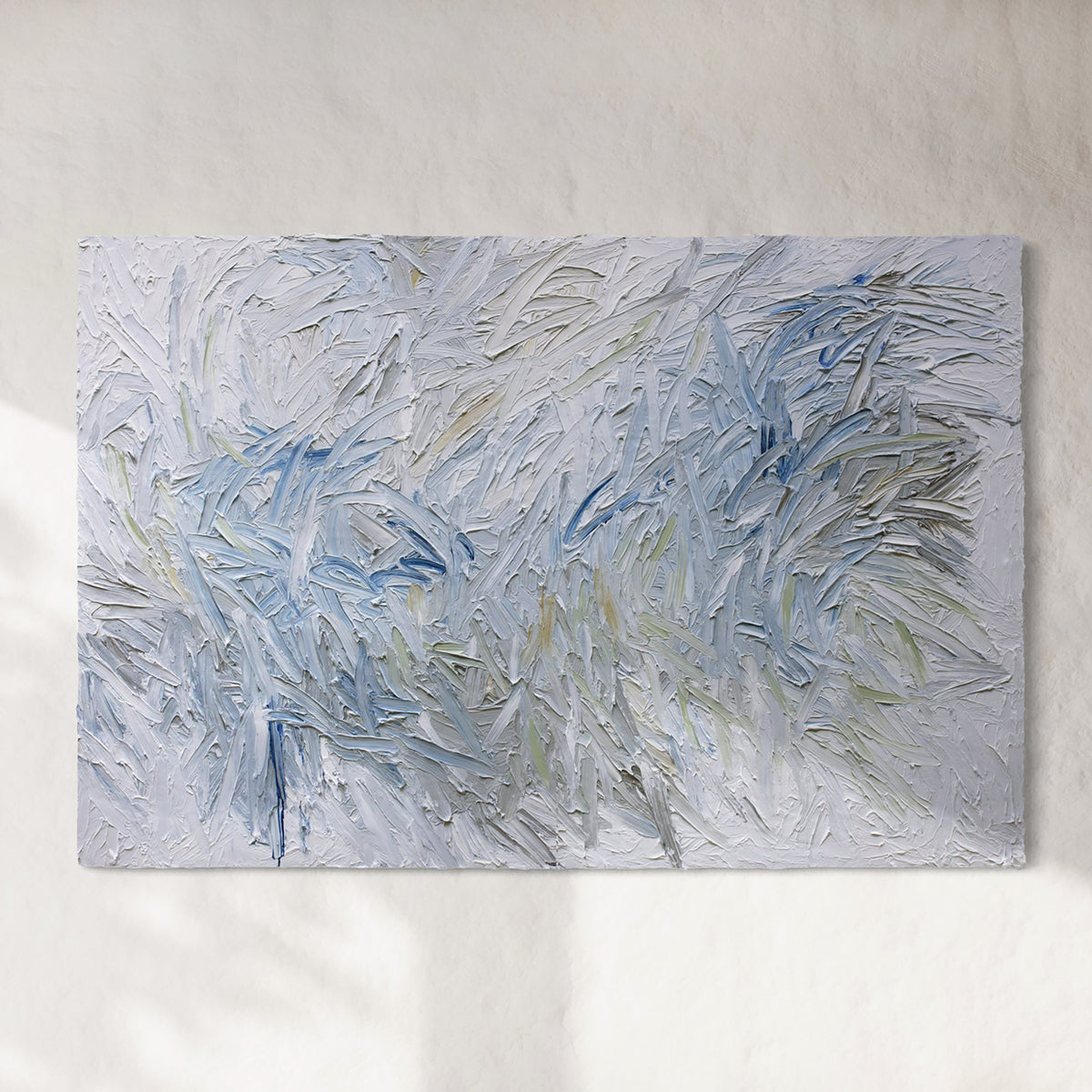 Original abstract painting by Teo Guererra with very textured blue and white brushstrokes hanging on a white sunlit wall.