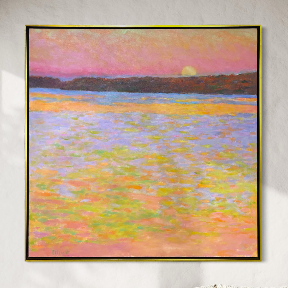 Framed painting of a sunset over water with a colorful sky hanging on a white wall.