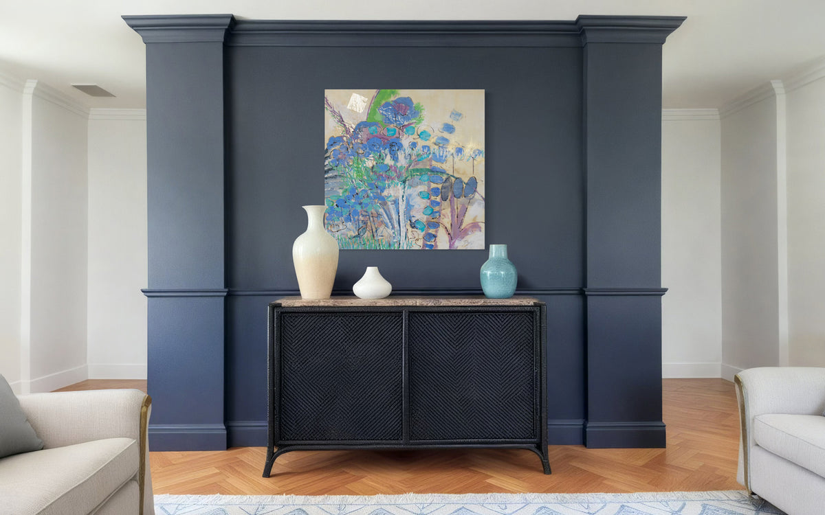 A blue and green abstracted encaustic painting hangs on a blue wall over a navy credenza.